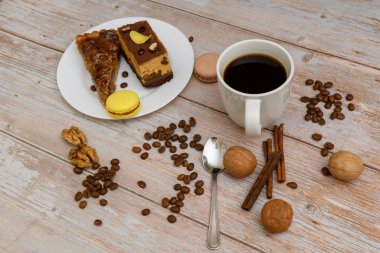Cup of coffee and two slices of cake and macaroons on the plate on wooden table