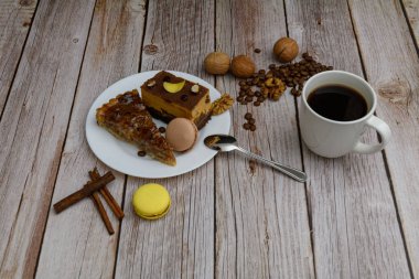 Cup of coffee and two slices of cake and macaroons on the plate on wooden table