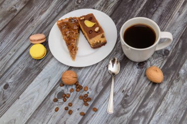 Cup of coffee and two slices of cake and macaroons on the plate on wooden table