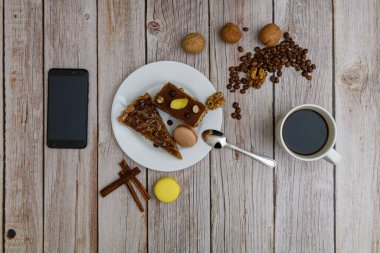 Cup of coffee and two slices of cake and macaroons on the plate on wooden table