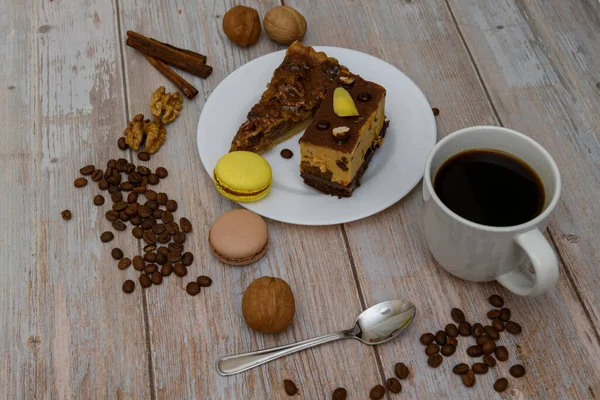 Cup of coffee and two slices of cake and macaroons on the plate on wooden table