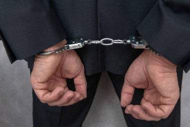 Arrested businessman or official in handcuffs with hands behind back. Corruption or economic crime concept.