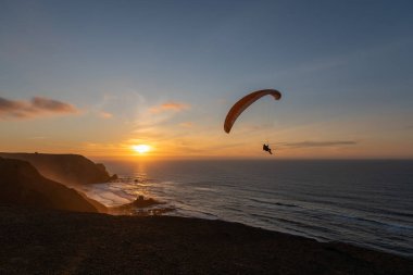 Paraglider flying over thesea shore at sunset. Paragliding sport concept.
