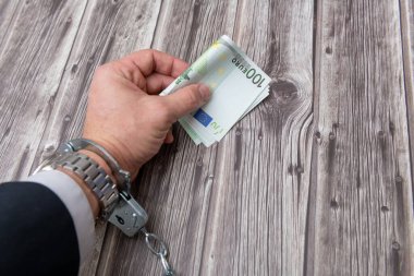 A man's hand in handcuffs and US dollars banknotes on wooden table. Corruption or economic crime concept.