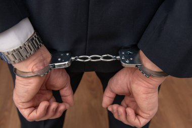 Arrested businessman or official in handcuffs with hands behind back. Corruption or economic crime concept.