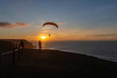 Paraglider flying over thesea shore at sunset. Paragliding sport concept.