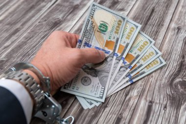 A man's hand in handcuffs and US dollars banknotes on wooden table. Corruption or economic crime concept.