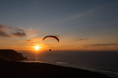 Paraglider flying over thesea shore at sunset. Paragliding sport concept.