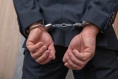 Arrested businessman or official in handcuffs with hands behind back. Corruption or economic crime concept.