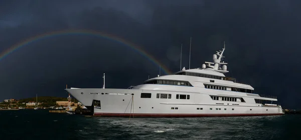 Luxury super yacht moored in marina. Beautiful rainbow on stormy sky.