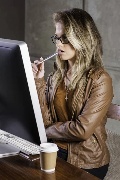 Schöne junge Frau sitzt an ihrem Schreibtisch und arbeitet an einem Computer. Stockfoto