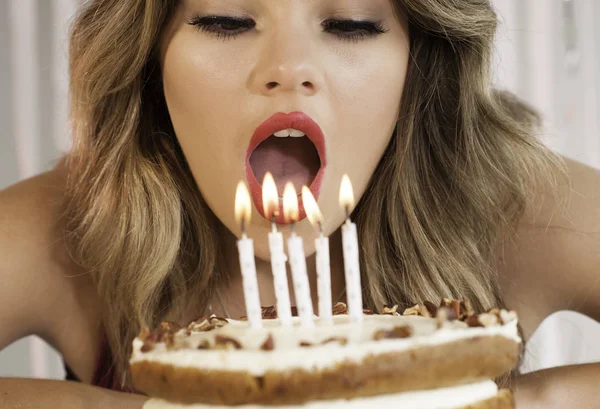Junges attraktives Geburtstagskind bläst Kerzen auf einer Torte aus Stockbild