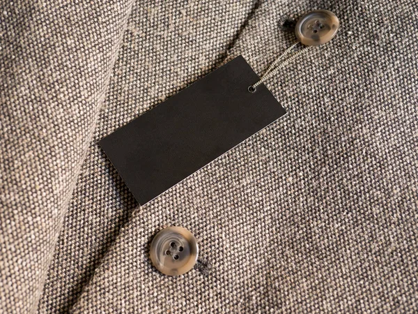 Blank black label price tag mockup on brown coat.