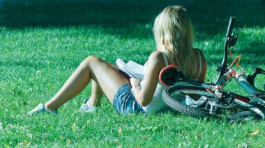 Sarışın kız bisikletçi kitap Şehir Parkı Savaşı'nda çim ile dinlenme