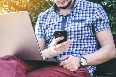 Genç adam akıllı telefon ve çalışma bir numara ile laptop dizlerinin üzerinde çevirir.