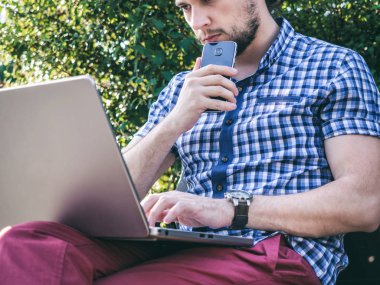 Telefon açık havada tutarak dizüstü bilgisayar ile sakallı genç hipster işadamı