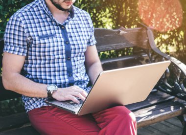 Genç adamın şehir parkında oturan ve onun laptopunda yazma gömlek giydiğini