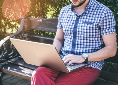 Genç şehir parkında oturan ve onun laptop, yazma gömlek giyen adam izle bileğine