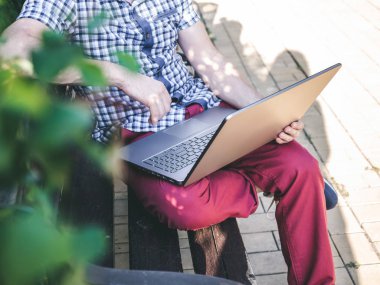 Genç adam oturma Park bankında ve onun Laptop üzerinde çalışıyor