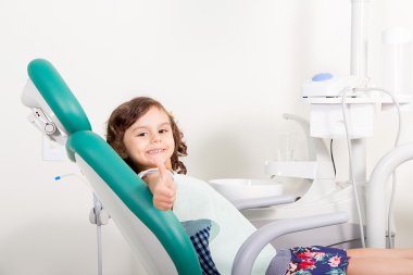 Diş kliniğinde ok imzalama gösterilen gülümseyen sevimli küçük kız