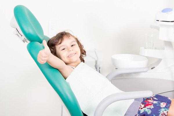 Cute little girl smiling showing Ok sign at dental clinic