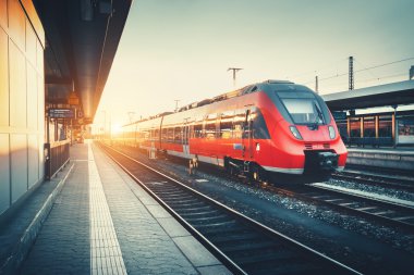 Railway station with beautiful modern red commuter train at suns
