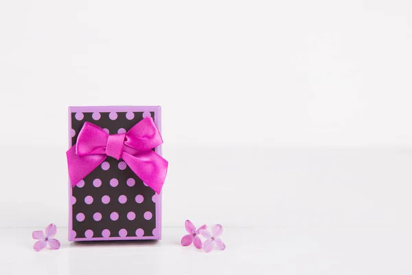 Caja de regalo púrpura rodeada de flores lila sobre fondo blanco — Foto de Stock