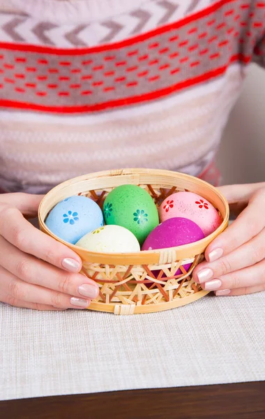 Manos femeninas sosteniendo cesta de mimbre con huevos de Pascua de colores — Foto de Stock