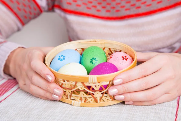 Manos femeninas sosteniendo cesta de mimbre con huevos de Pascua de colores — Foto de Stock