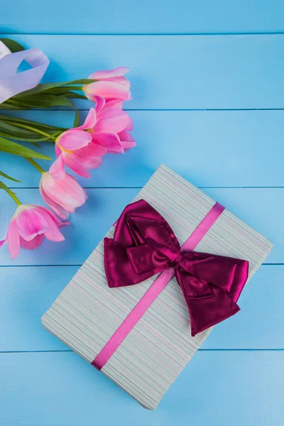 Ramo de tiernos tulipanes rosados con caja de regalo en respaldo de madera azul — Foto de Stock