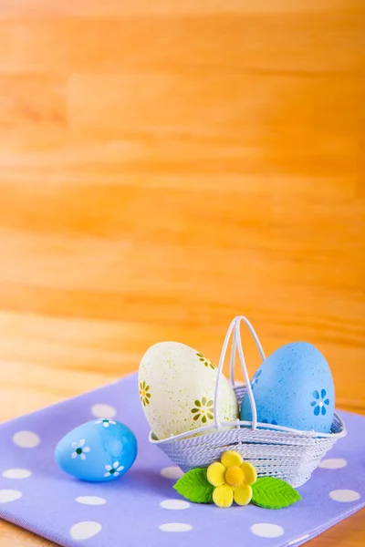 Uova di Pasqua colorate in cesto con fiore su tessuto su b di legno — Foto Stock