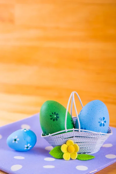 Uova di Pasqua colorate in cesto con fiore su tessuto su b di legno — Foto Stock