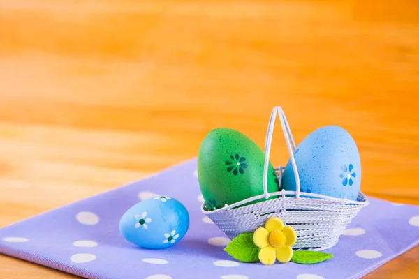 Colorful Easter eggs in basket with flower on fabric on wooden b — Stock Photo, Image