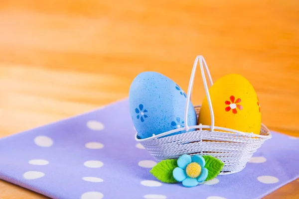 Uova di Pasqua colorate in cesto con fiore su tessuto su b di legno — Foto Stock