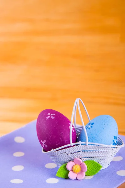 Uova di Pasqua colorate in cesto con fiore su tessuto su b di legno — Foto Stock