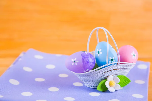 Uova di Pasqua colorate in cesto con fiore su tessuto su b di legno — Foto Stock