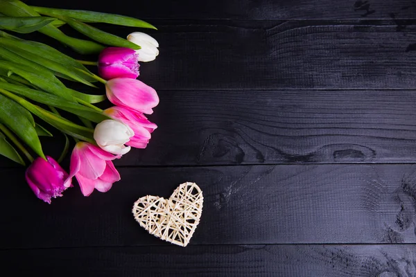 Bouquet di teneri tulipani rosa e cuore di vimini su b di legno nero — Foto Stock