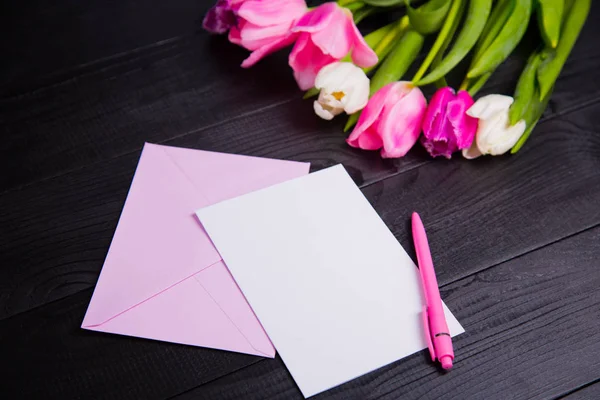 Bouquet of tender pink tulips and clear paper on black wooden ba — Stock Photo, Image