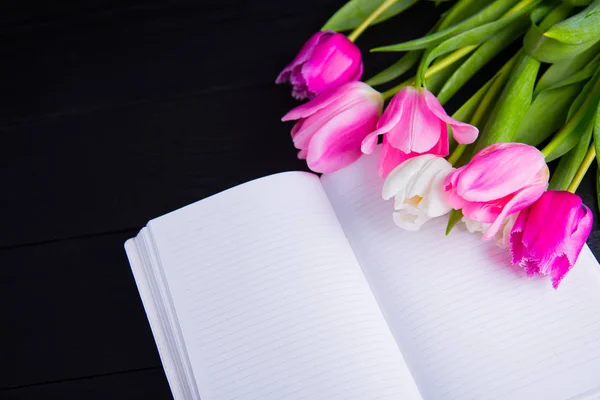 Buquê de tulipas rosa concurso e caderno aberto em madeira preta — Fotografia de Stock