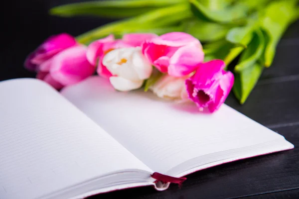 Buquê de tulipas rosa concurso e caderno aberto em madeira preta — Fotografia de Stock