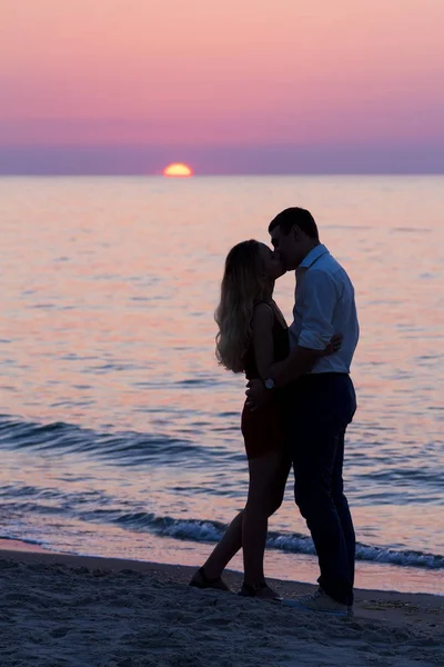 Siluetas oscuras de pareja joven besándose en la playa al amanecer — Foto de Stock