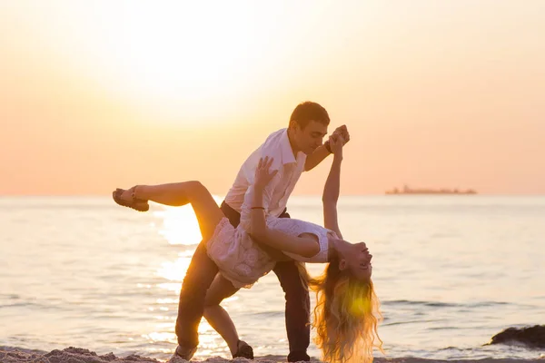 Pareja joven bailando en la playa al amanecer dorado — Foto de Stock