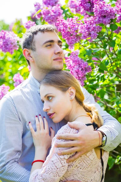 Joven pareja romántica de pie entre los arbustos lila en primavera ga — Foto de Stock