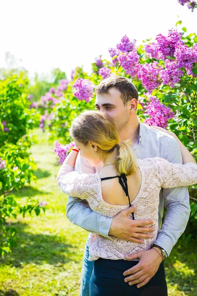 Joven pareja romántica de pie entre los arbustos lila en primavera ga — Foto de Stock