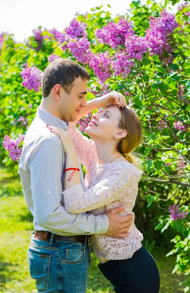 Joven pareja romántica de pie entre los arbustos lila en primavera ga — Foto de Stock