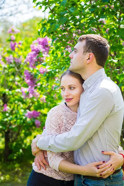 Joven pareja romántica de pie entre los arbustos lila en primavera ga — Foto de Stock