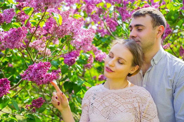 Joven pareja romántica de pie entre los arbustos lila en primavera ga — Foto de Stock