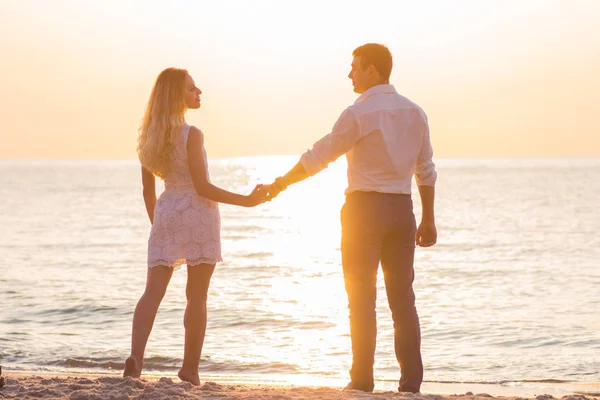 Hermosa pareja romántica joven cogida de la mano en la playa en rayos — Foto de Stock