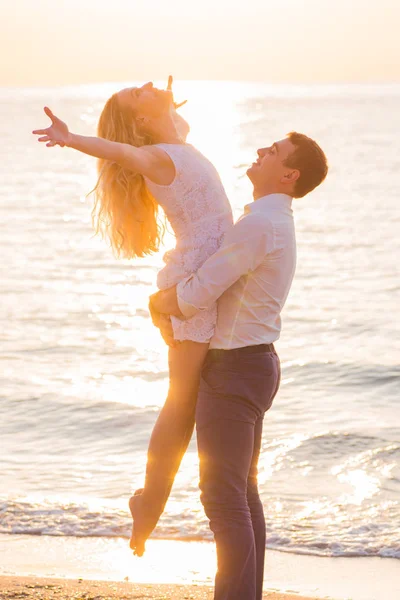 Hermosa pareja romántica joven en la orilla del mar en los rayos del sol naciente — Foto de Stock