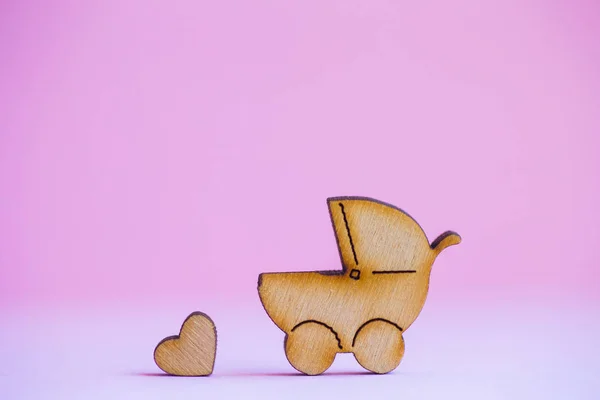 Drewniane ikony baby buggy i serduszko na różowym tle — Zdjęcie stockowe